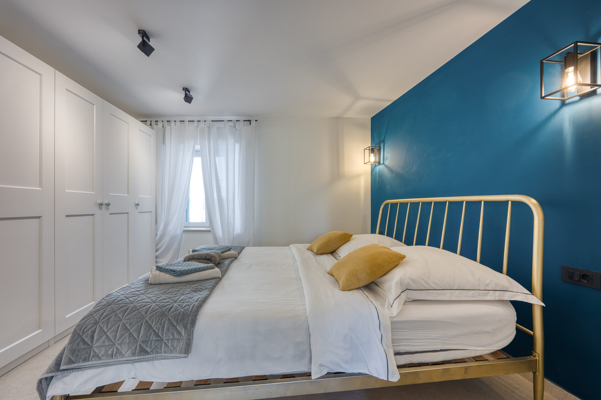 Schlafzimmer mit goldenem Bettgestell vor petrolfarbener Akzentwand